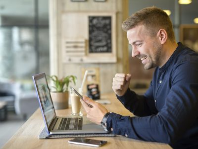 Happy freelancer with tablet and laptop computer in coffee shop.